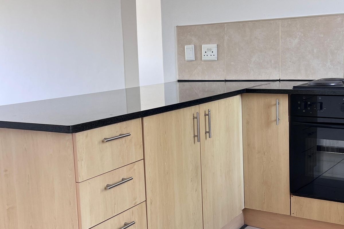 A clean, functional kitchen featuring light wood-finish cabinetry, black granite countertops, built-in oven, and neutral ceramic floor tiles.
