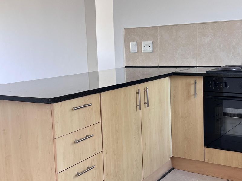 A clean, functional kitchen featuring light wood-finish cabinetry, black granite countertops, built-in oven, and neutral ceramic floor tiles.