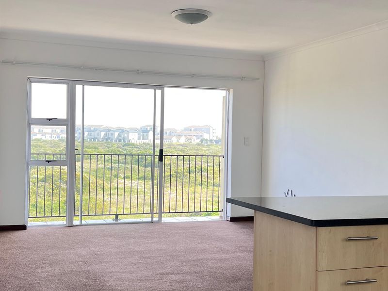 Open plan living area featuring a kitchen island, carpeted lounge space, and sliding glass doors leading to a balcony with scenic views.