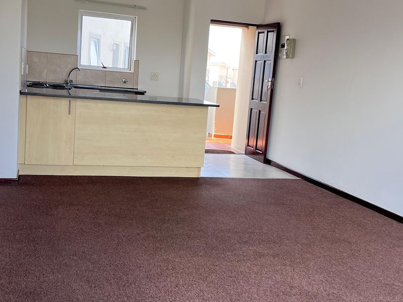 An open-plan living area featuring a compact kitchen with built-in cabinetry, granite countertops, and a hob, finished with carpet flooring.