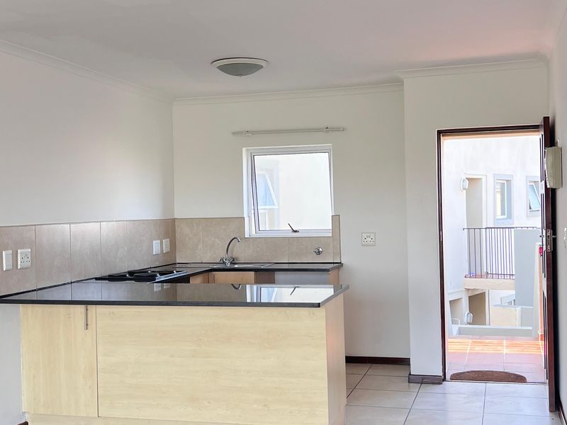 Open-plan kitchen area featuring granite countertops, built-in hob, and tiled flooring, with direct access to an exterior balcony.