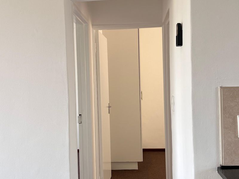 A clean, neutral hallway featuring carpeted flooring and built-in storage cupboards, providing access to adjacent rooms within the apartment.