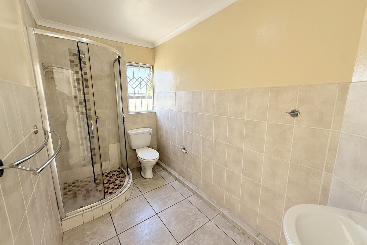A functional bathroom featuring a corner shower enclosure, toilet, and washbasin with neutral wall and floor tiling.