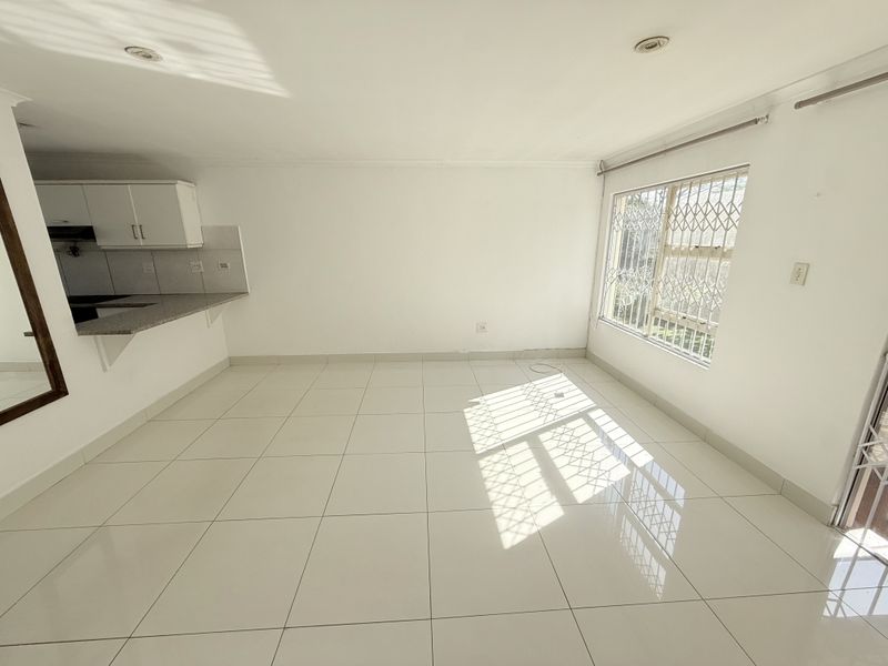 Bright open-plan living area featuring tiled floors, recessed lighting, and an integrated kitchen with granite countertops and security fixtures on windows.
