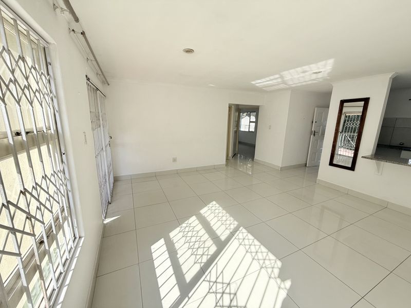 Bright and spacious open-plan living area featuring neutral tiled flooring, security gates, and a convenient breakfast counter connecting to the kitchen space.