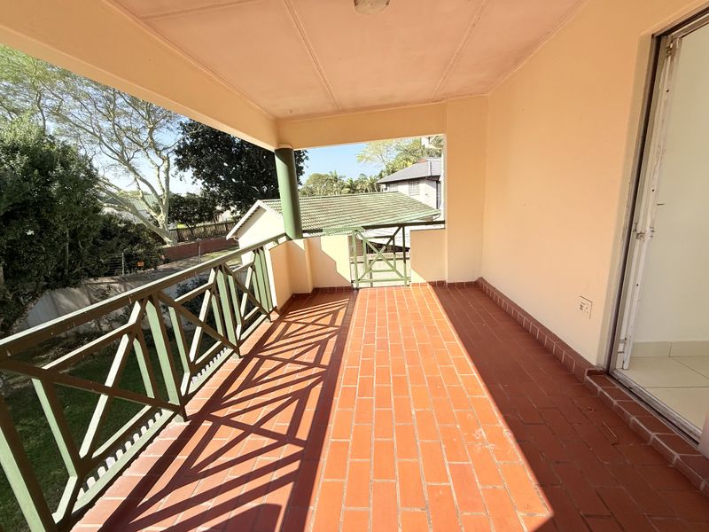A spacious covered balcony featuring terracotta tile flooring and a metal balustrade, offering an open outdoor area accessible via a sliding glass door.