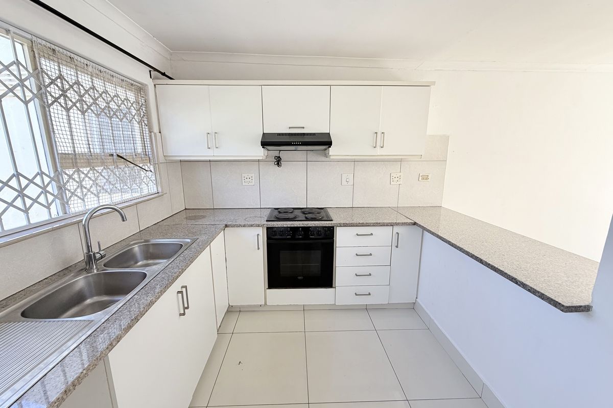A functional kitchen featuring white cabinetry, granite countertops, a double sink, and a built-in electric stove with an extractor fan.