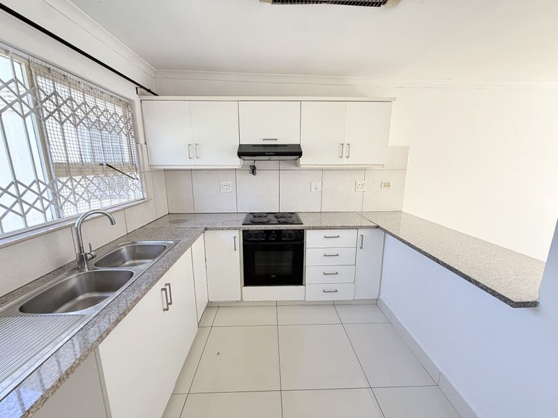 A functional kitchen featuring white cabinetry, granite countertops, a double sink, and a built-in electric stove with an extractor fan.