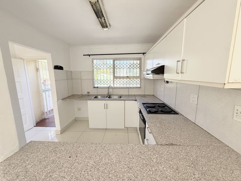 A functional kitchen featuring granite countertops, built-in cabinetry, an electric hob with extractor fan, and tiled flooring, offering a clean and practical workspace.