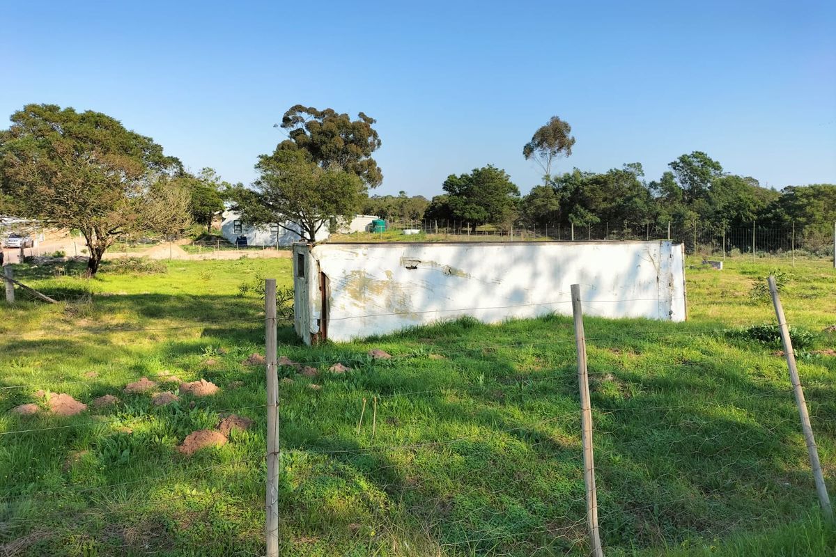 A vacant residential plot featuring a wire fence and a weathered metal storage container situated on a grassy landscape.