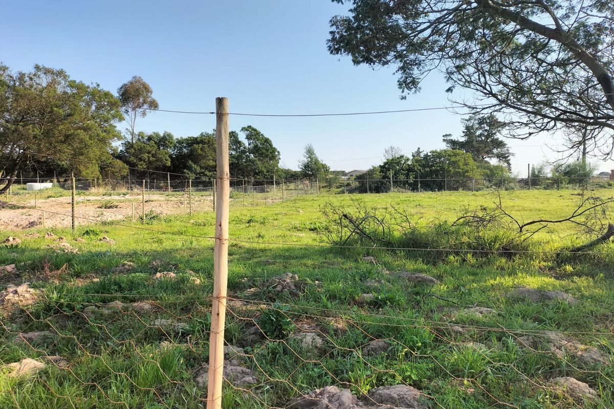 A view of a vacant residential plot featuring grassy terrain and perimeter wire fencing with wooden posts.