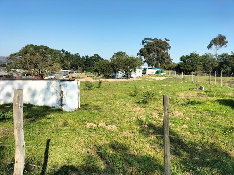 A view of a vacant residential plot featuring wire fencing and wooden posts, with open grassy land and mature trees in the background.