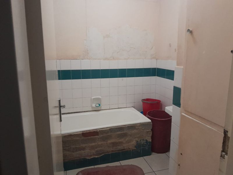 A dated bathroom featuring a bathtub with an unfinished brick base and wall damage, requiring renovation and cosmetic updates to improve functionality and aesthetics.