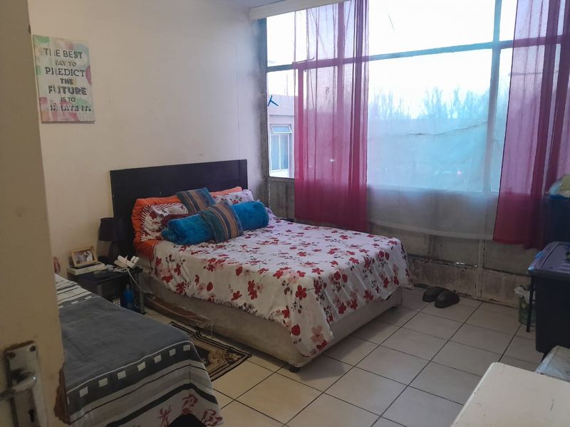 A bedroom featuring tiled flooring and a large window, requiring cosmetic updates to improve the overall condition and aesthetic appeal.