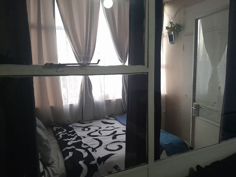 A bedroom view captured through a window frame, showing a compact sleeping area with natural light.