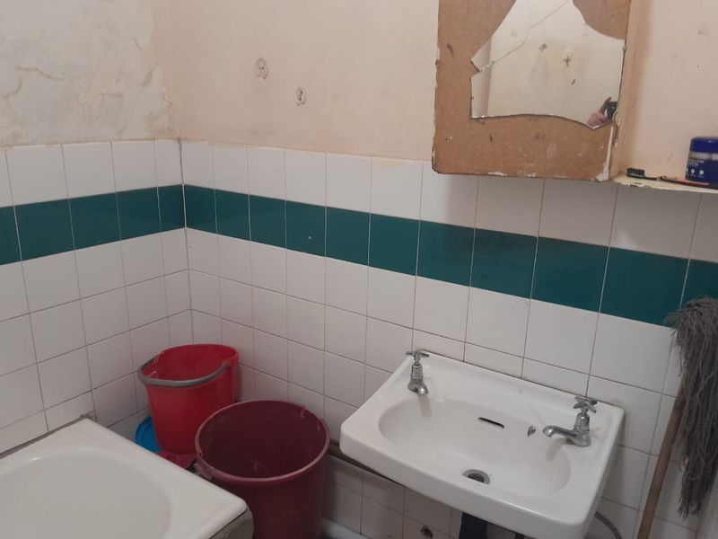 A dated bathroom featuring a wall-mounted basin with dual-handle taps and tiled splashbacks, requiring significant cosmetic renovation and repair to wall finishes.