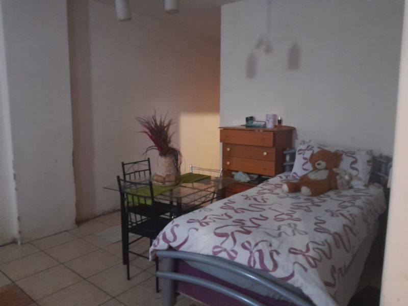 A bedroom featuring tiled flooring and plain walls, currently furnished with a single bed and small dining set.