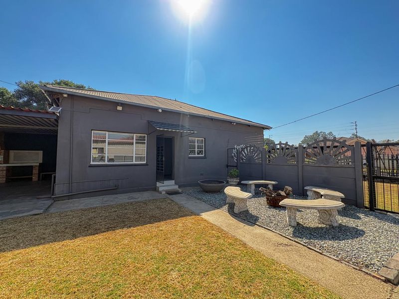Rear exterior view of the property featuring a paved patio area, built-in braai, and a low-maintenance garden with a precast boundary wall.