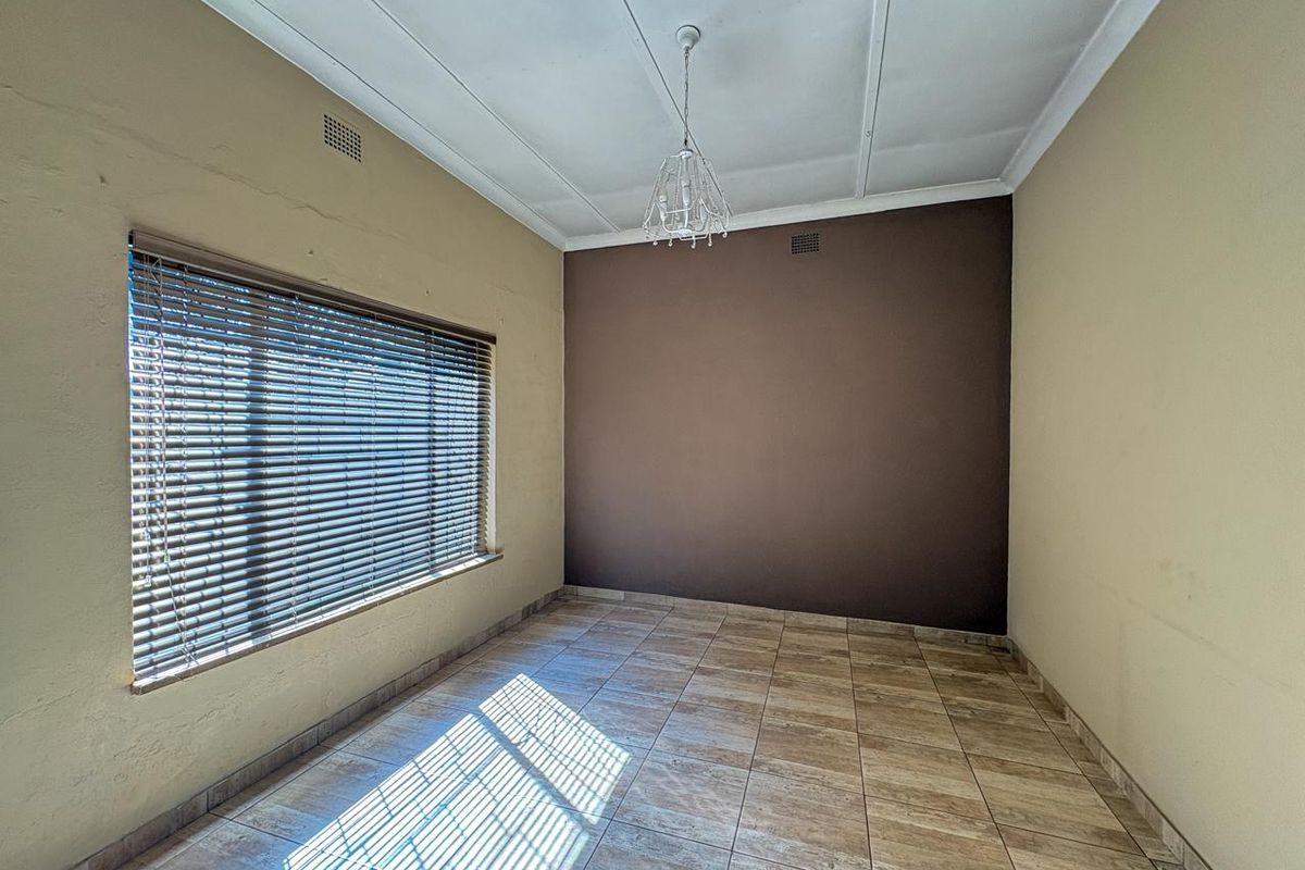 An empty bedroom featuring tiled flooring, a large window with venetian blinds, and a central pendant light fixture.