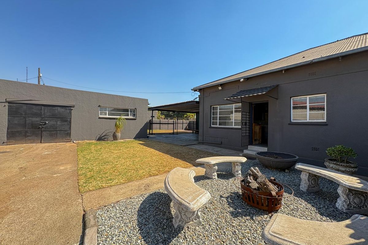 Rear exterior view featuring a paved driveway, a detached garage, a small lawn area, and a gravel courtyard with built-in stone seating.