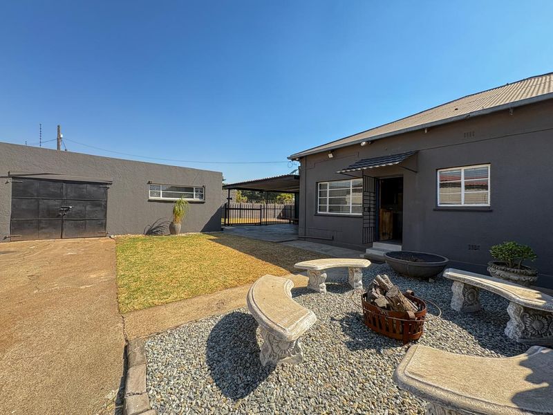 Rear exterior view featuring a paved driveway, a detached garage, a small lawn area, and a gravel courtyard with built-in stone seating.