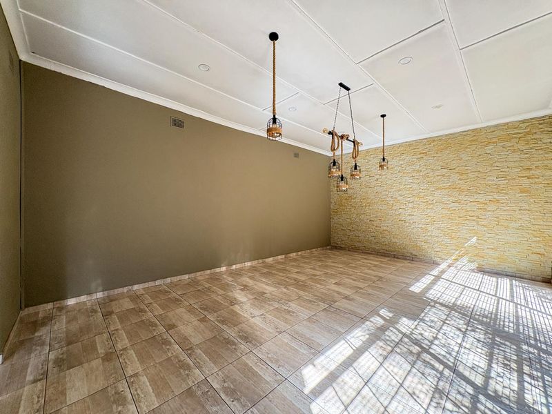 An empty living area featuring tiled flooring, a textured stone feature wall, and decorative pendant lighting fixtures.