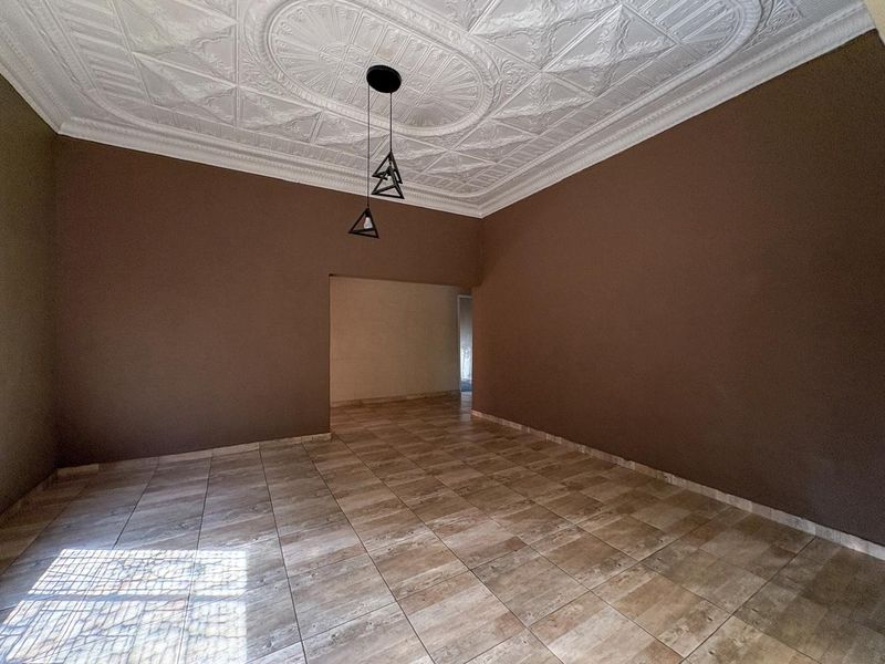 An empty living room featuring decorative plaster ceiling detailing, ceramic floor tiles, and modern pendant lighting.