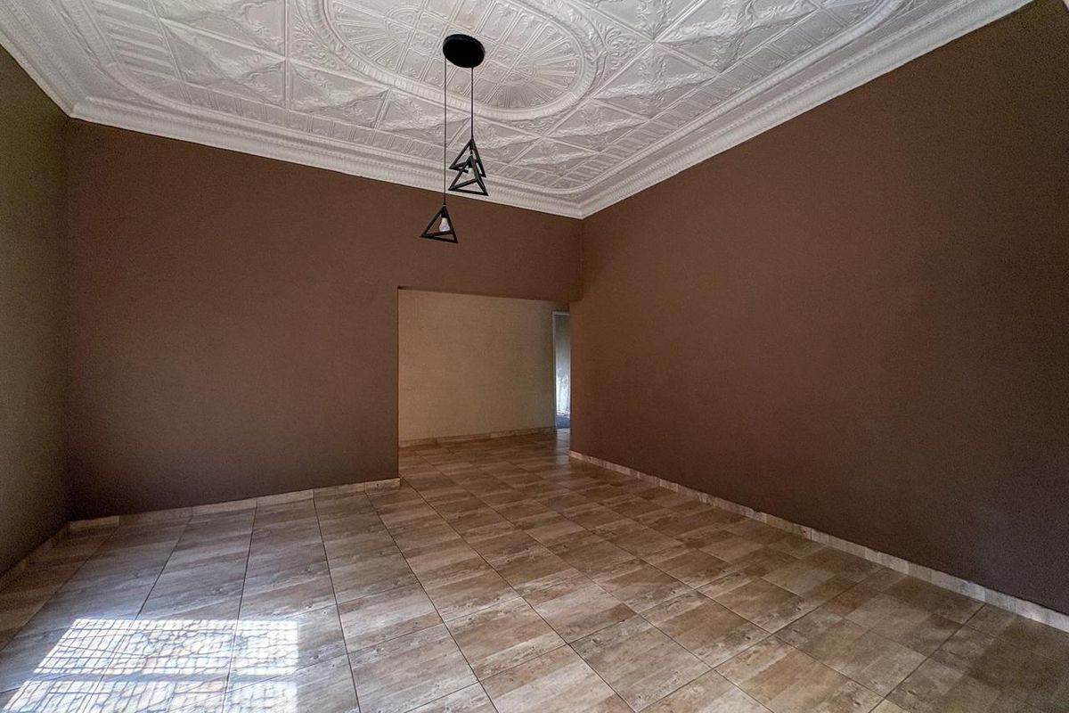 An empty living room featuring decorative plaster ceiling detailing, ceramic floor tiles, and modern pendant lighting.