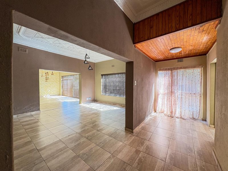 Spacious open-plan living area featuring tiled flooring, a combination of ornate plaster and timber-paneled ceilings, and large sliding doors providing natural light.
