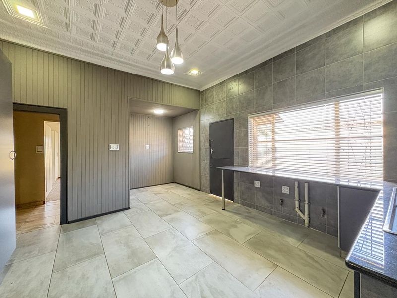 A spacious, empty kitchen area featuring tiled flooring, a decorative pressed metal ceiling, and a built-in counter with integrated plumbing connections.