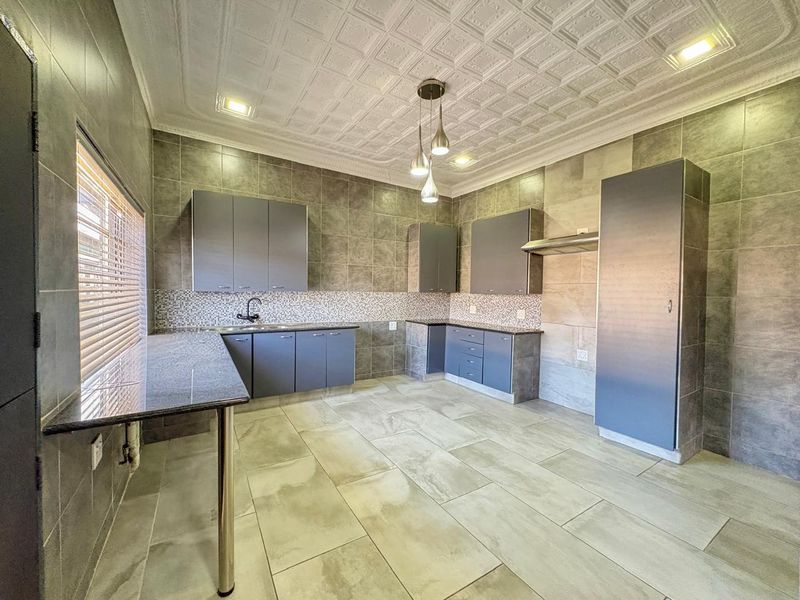 Modern kitchen featuring grey built-in cabinetry, granite countertops, tiled walls, and decorative ceiling tiles with recessed lighting.