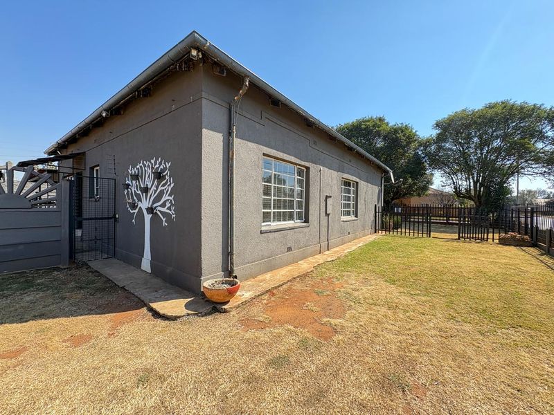 Rear view of the property featuring plastered exterior walls, security bars on windows, and a fenced garden area with a concrete pathway.