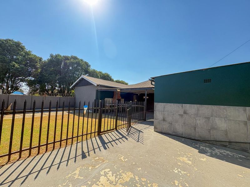 Rear exterior view featuring a covered patio with a built-in brick braai, concrete driveway, and fenced garden area.