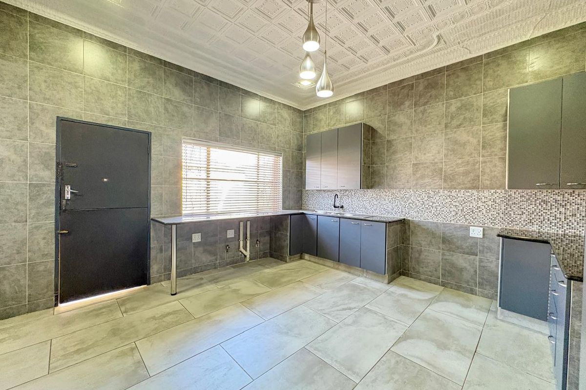 A modern, spacious kitchen featuring grey cabinetry, granite countertops, tiled walls, and decorative ceiling tiles, offering a clean and functional workspace.