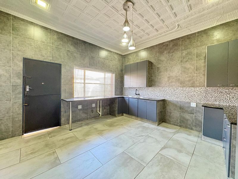 A modern, spacious kitchen featuring grey cabinetry, granite countertops, tiled walls, and decorative ceiling tiles, offering a clean and functional workspace.