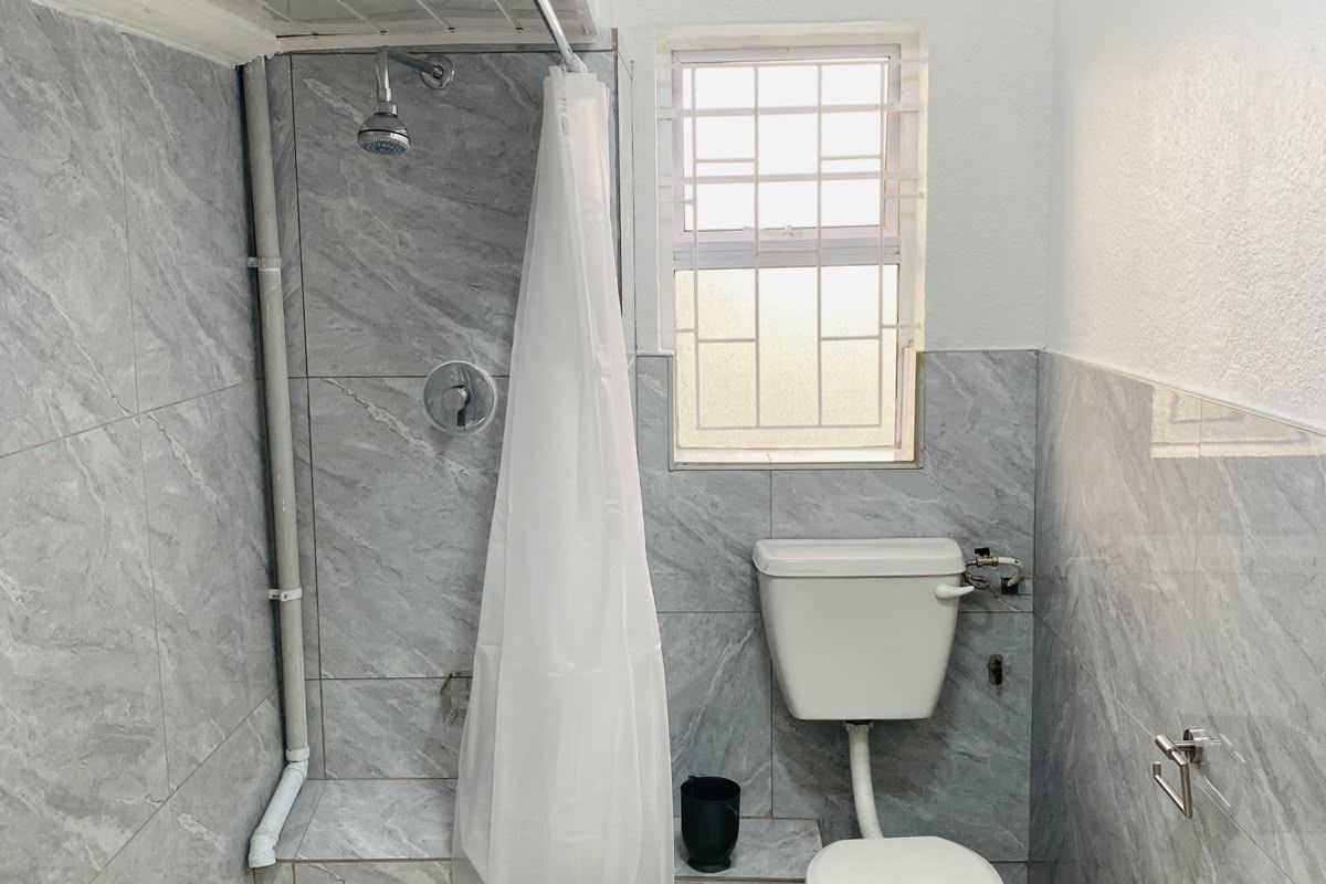 A compact bathroom featuring grey marble-effect wall tiles, a shower area, and a standard toilet with a window for natural light.