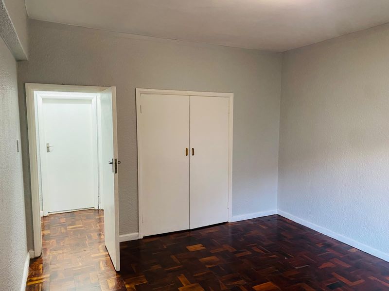 A bright, empty bedroom featuring classic parquet flooring and a built-in wardrobe, offering a clean canvas for personalization.