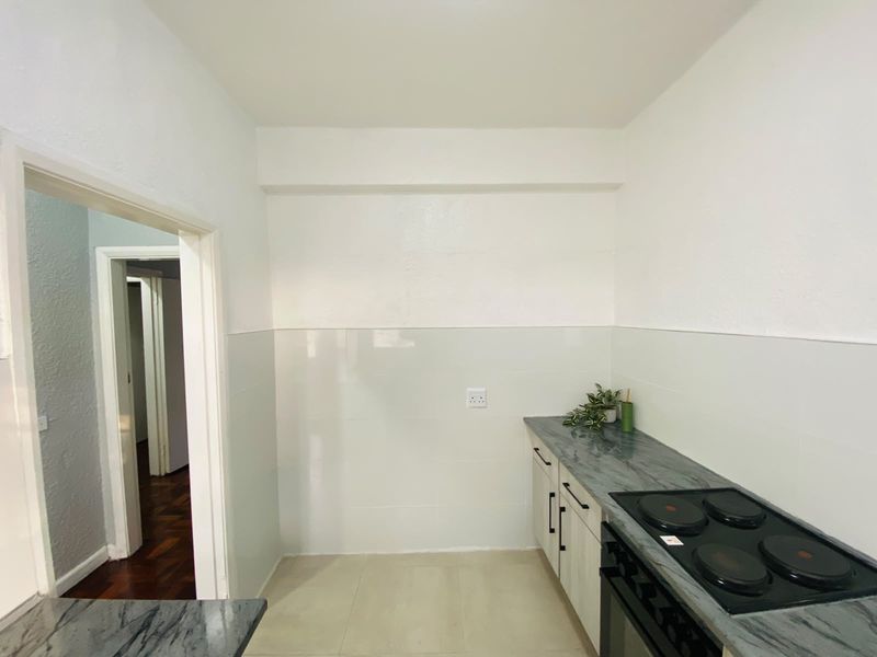 A clean, functional kitchen area featuring built-in cabinetry, stone countertops, and an integrated electric hob and oven with tiled splashbacks.