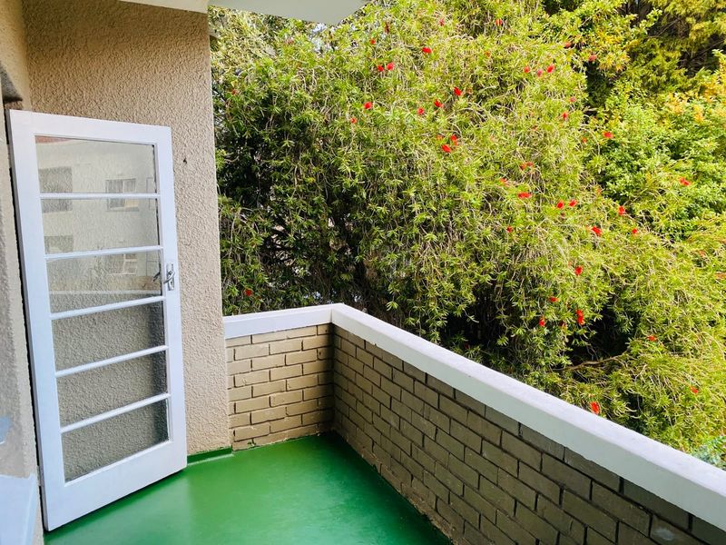 A private balcony featuring a painted concrete floor, brick balustrade, and direct access through a glass panel door, overlooking lush greenery.