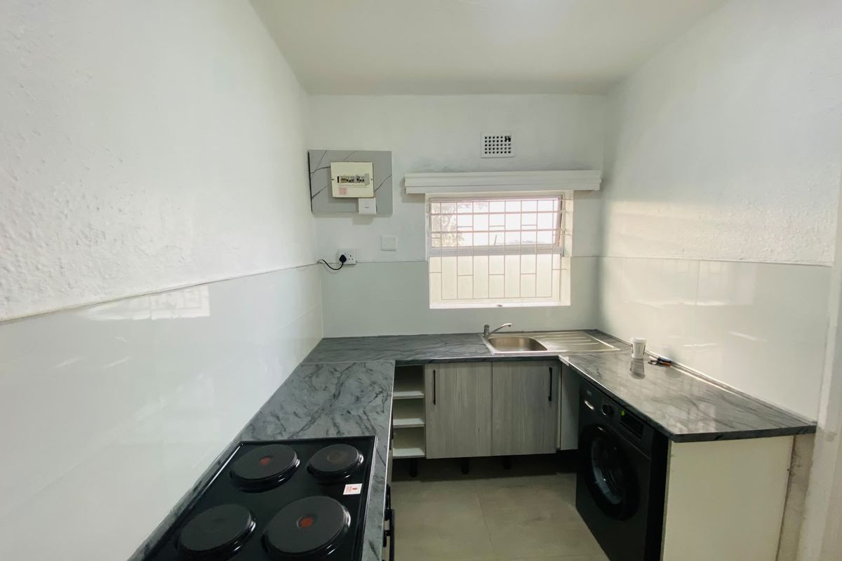 A clean, functional kitchen featuring built-in cabinetry, laminate countertops, a stainless steel sink, and an integrated electric hob with tiled splashbacks.
