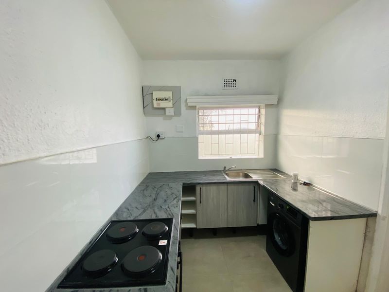 A clean, functional kitchen featuring built-in cabinetry, laminate countertops, a stainless steel sink, and an integrated electric hob with tiled splashbacks.