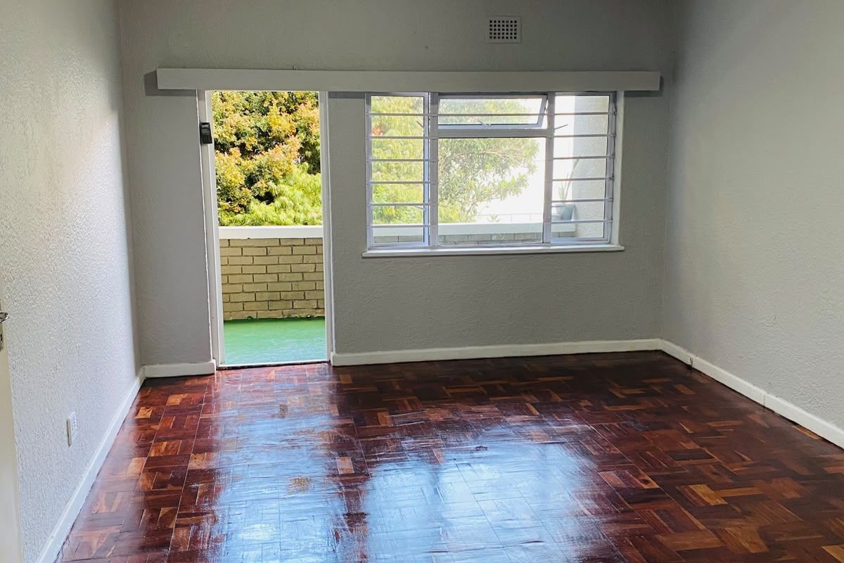 An empty living room featuring polished parquet flooring, large windows with security bars, and direct access to an outdoor balcony area.