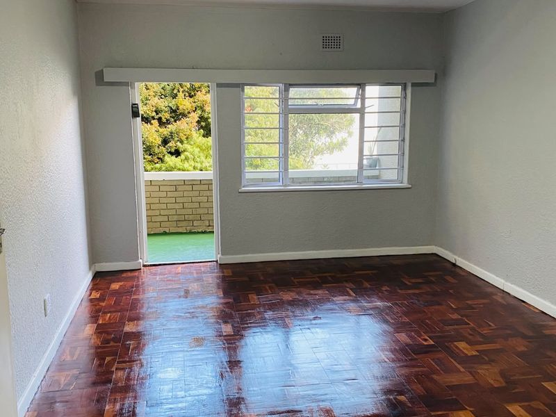 An empty living room featuring polished parquet flooring, large windows with security bars, and direct access to an outdoor balcony area.