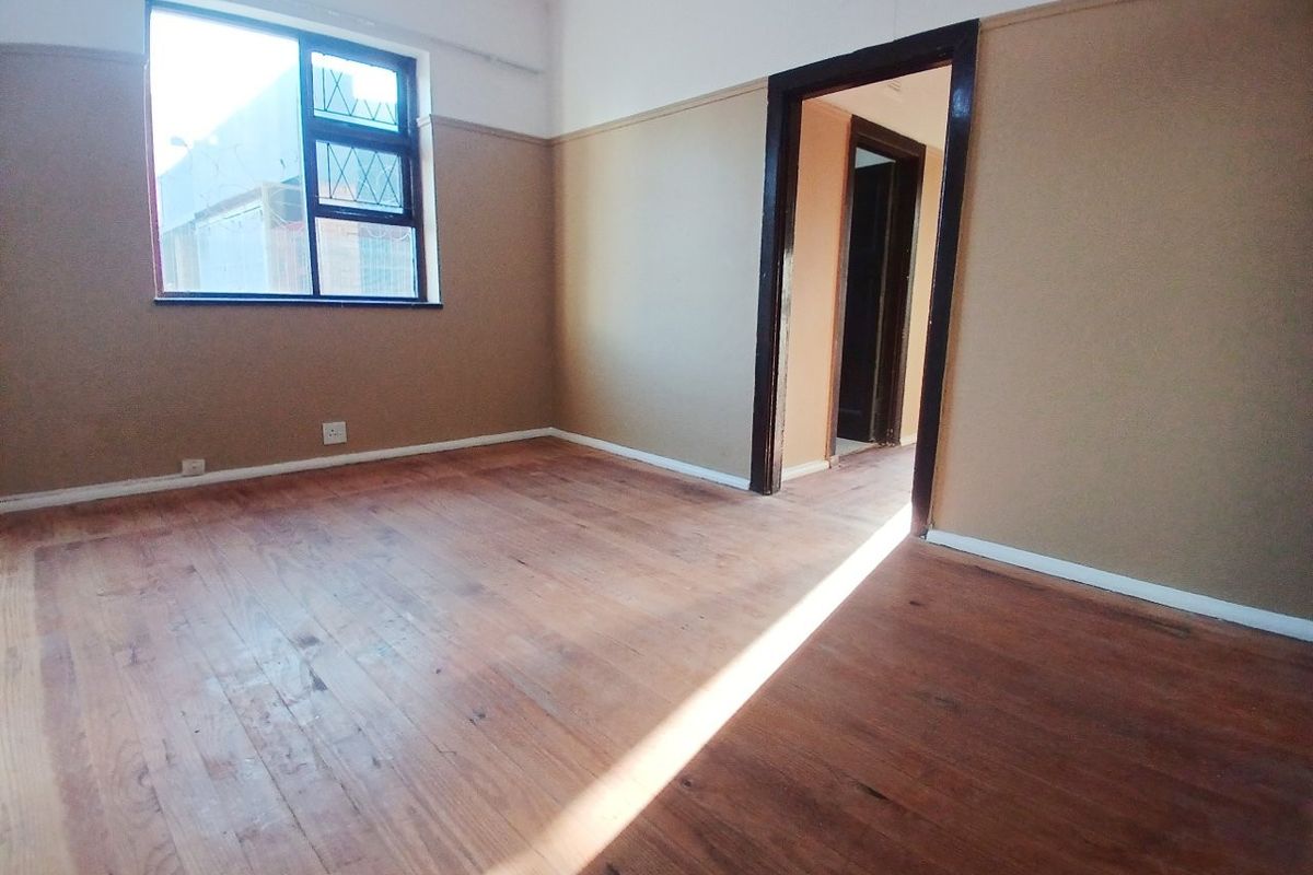 An empty bedroom featuring original timber flooring, neutral wall paint, and a steel-framed window, offering a blank canvas for renovation.
