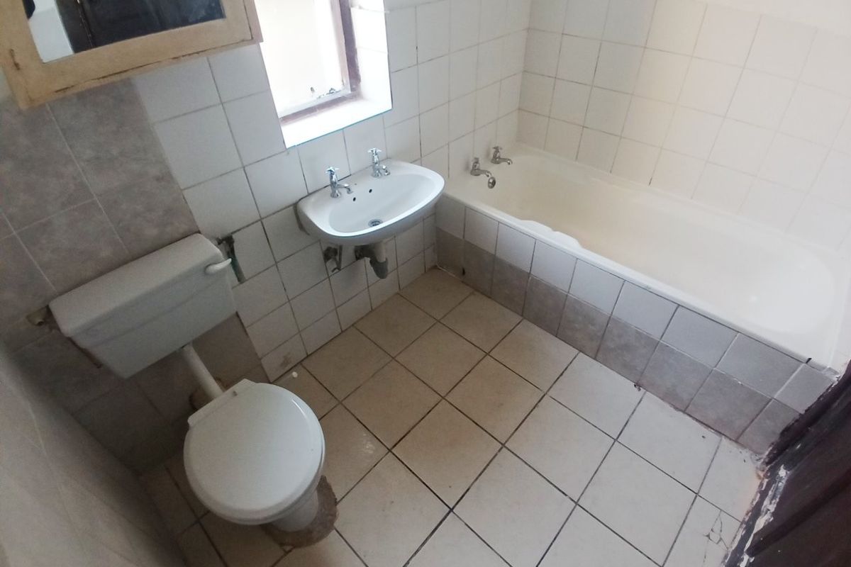 A dated bathroom featuring a standard bathtub, wall-mounted basin, and toilet with ceramic tiling throughout, requiring cosmetic updates and repairs.