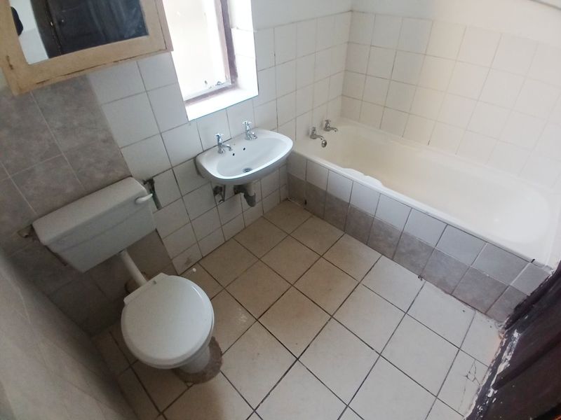 A dated bathroom featuring a standard bathtub, wall-mounted basin, and toilet with ceramic tiling throughout, requiring cosmetic updates and repairs.