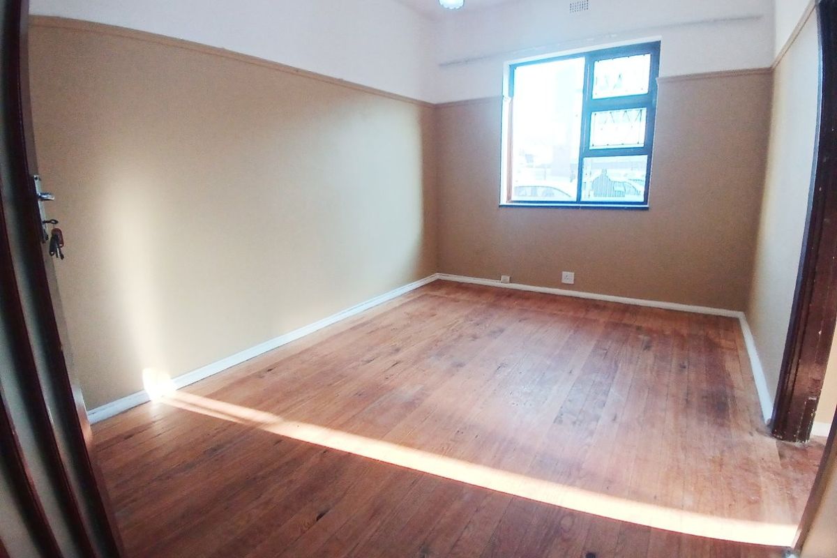 An empty bedroom featuring original hardwood flooring, a casement window, and two-tone wall finishes with a picture rail.