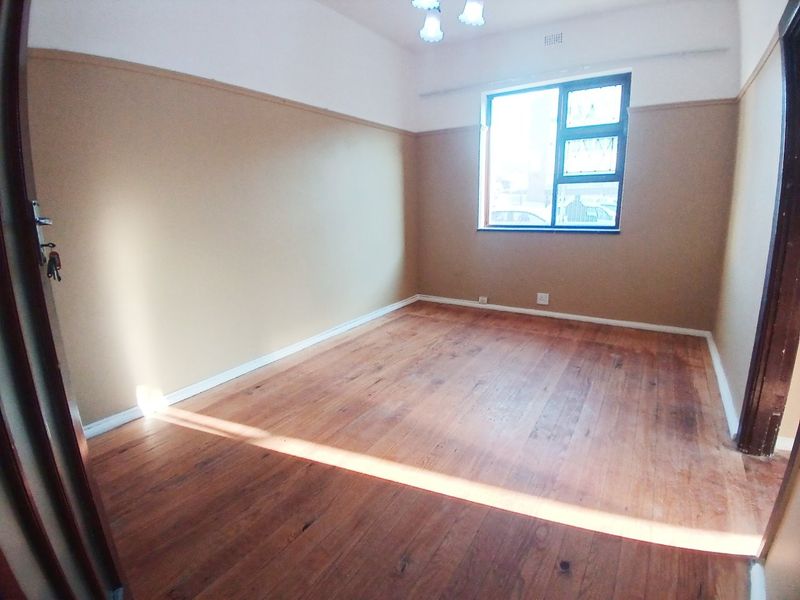 An empty bedroom featuring original hardwood flooring, a casement window, and two-tone wall finishes with a picture rail.