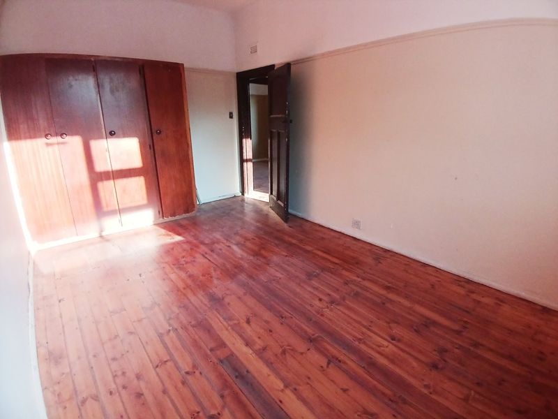 An empty bedroom featuring original wooden flooring, built-in timber cupboards, and a classic picture rail, offering a blank canvas for renovation.