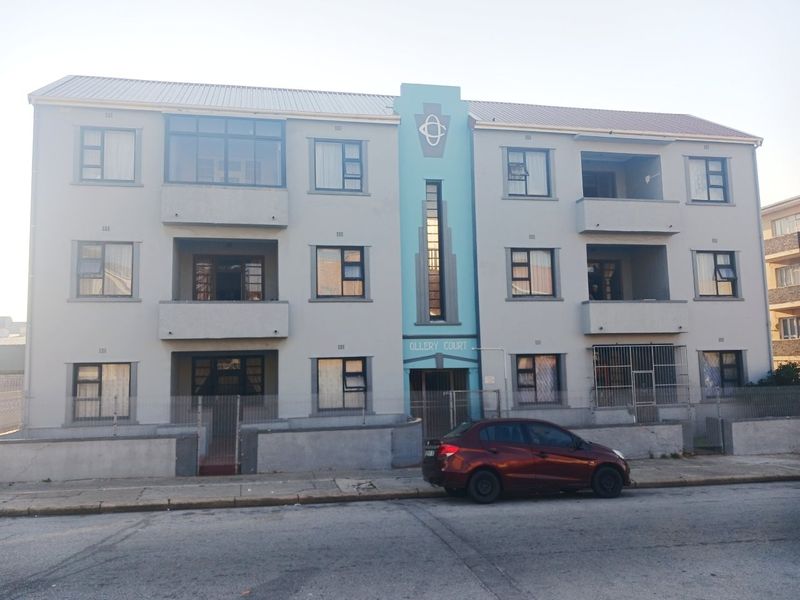 Front elevation of Ollery Court, a multi-story apartment building featuring a central entrance, balconies, and secure perimeter fencing.